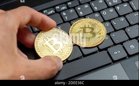 Hand placing two bitcoin gold coin symbols on a modern laptop keyboard. Bit coin cryptocurrency logo, crypto trading market Stock Photo