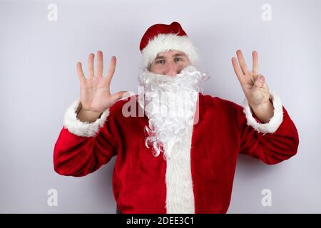 Man dressed as Santa Claus standing over isolated white background showing and pointing up with fingers number eight while smiling confident and happy Stock Photo