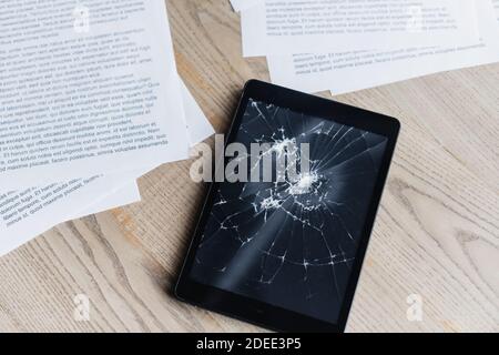 Top view of smashed digital tablet with documents on textured wooden background Stock Photo