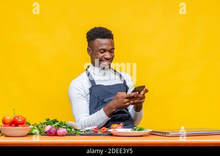 young african chef smiling while using his phone, on social media Stock Photo