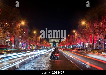 Young couple on Champs Elysees avenue and the Arc de Triomphe decorated with red Christmas lights at night  in Paris, France. Christmas holidays, wint Stock Photo