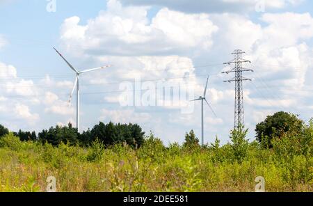 Two wind turbines and power lines in a green field, country landscape shot, sunny weather. Green energy, ecology, alternative renewable energy sources Stock Photo