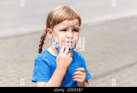 Single tired, unhappy and worried anxious little girl, child taking off a protective face mask, young school kid portrait. Covid 19, corona virus Stock Photo