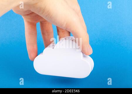 Hand holding a white cloud prop, placing, putting down a white 3d cloud symbol on blue background. Simmple cloud server online storage, internet data Stock Photo