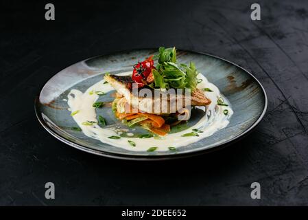 grilled cod fillet with vegetables and sauce on a black background Stock Photo