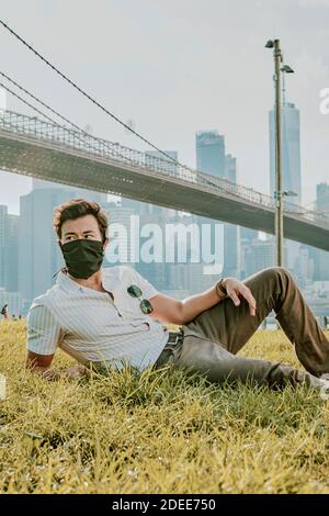 Young man sitting in park wearing face mask. Stock Photo