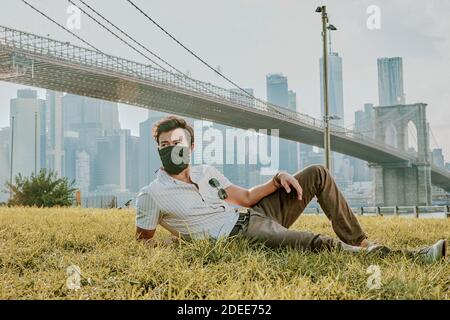 Young man sitting in park wearing face mask. Stock Photo