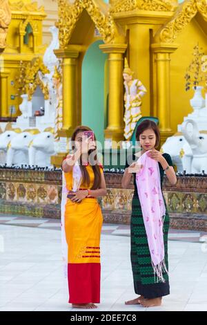 Pretty young women tourists with thanaka on cheeks taking photos at Shwedagon Pagoda, Yangon, Myanmar (Burma), Asia in February Stock Photo