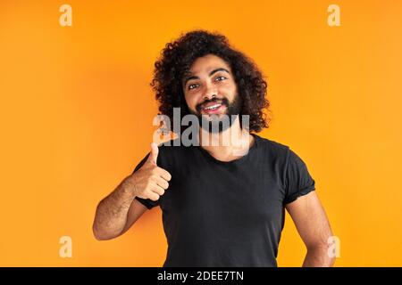 portrait of an excited bearded arab man standing isolated over yellow background, good job. he shows thumbs up at camera Stock Photo