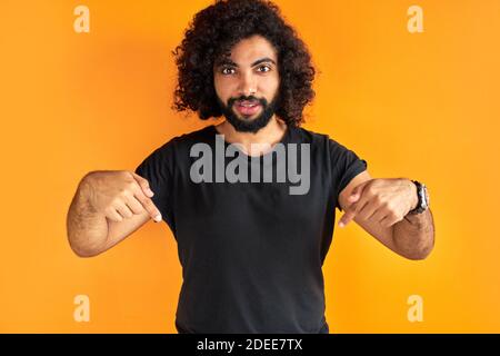 serious cury man points down with index finger, dressed in casual clothes, shows free space for your advertising content Stock Photo