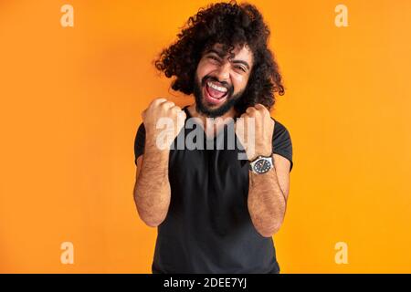 happy bearded man celebrate his winning, smile, curly guy shine with happiness, victory concept. isolated orange background Stock Photo