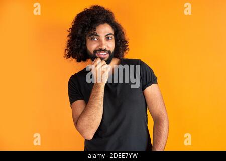portrait of pleased arab man isolated in studio, handsome guy in casual wear posing at camera, has black long curly hair, calm male of indian or arabi Stock Photo