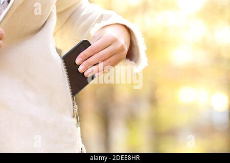 Close up of woman hand keeping smart phone in a jacket pocket in fall season in a park Stock Photo
