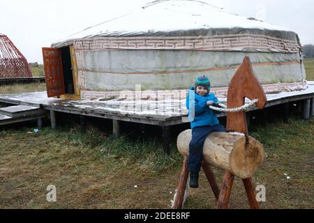 Child sitting on wooden horse in front of Yakut yurt Stock Photo