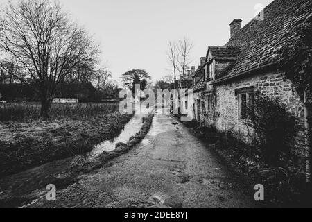 View of the Cotswold village of Bibury, showing the famous row of former 14the century weavers cottages in Arlington Row on a dark wet day Stock Photo