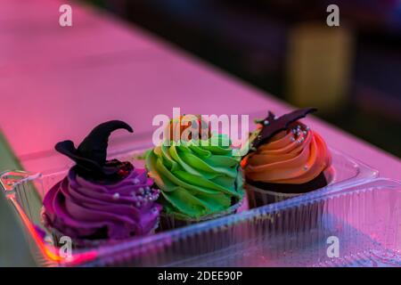 Colorful cakes for Halloween. Set of birthday cakes in a plastic box in neon lighting. Beautiful pumpkin, witch and bat cake. Soft evening lighting. H Stock Photo