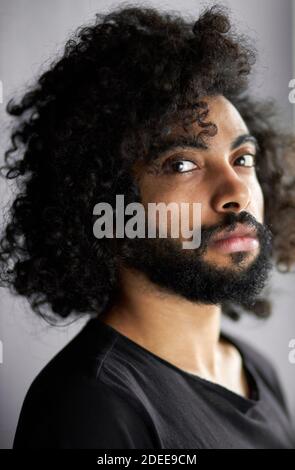 close-up portrait of curly indian male having deep look, handsome guy in casual black t-shirt is in contemplation Stock Photo