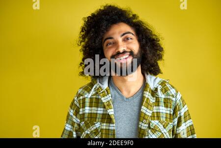 portrait of positive cheerful curly arabian man in casual shirt laughing isolated on green background, young bearded male shine with happiness Stock Photo