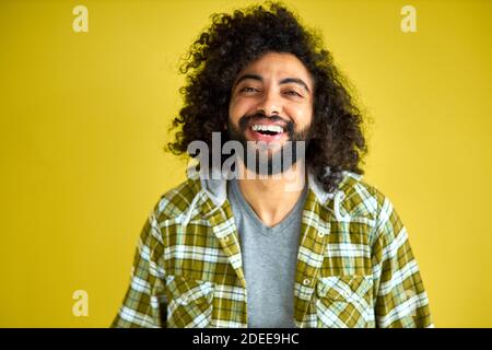 portrait of positive cheerful curly arabian man in casual shirt laughing isolated on green background, young bearded male shine with happiness Stock Photo