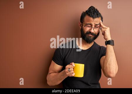 sleepy arabic man with cup of coffee in the morning isolated on brown background, handsome guy want to sleep Stock Photo