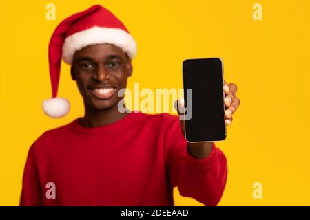 Mockup Of African Guy In Santa Hat Holding Smartphone With Black Screen Stock Photo