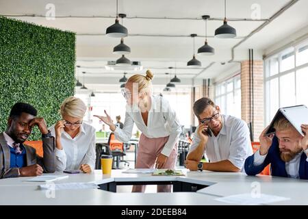 team of sad frustrated employees receiving rebuke by shouting female executive, workers are suffering from bad attitude from angry boss Stock Photo