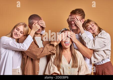 cheerful group of youth closing eye of each other having fun isolated over brown background Stock Photo