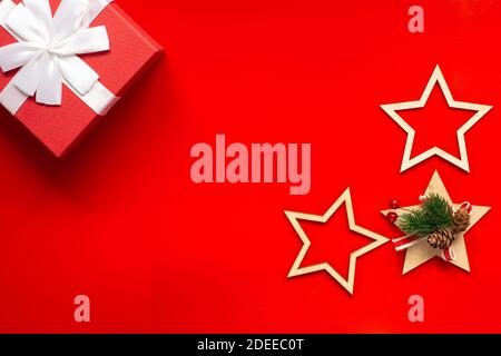 A red gift box with a white bow, wooden Christmas tree decorations in the form of stars on a red background. Stock Photo