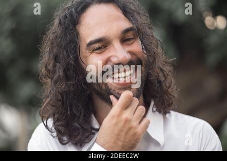 A young Hispanic bearded man with long hair posing at the camera outdoors Stock Photo