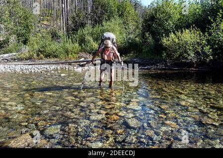 WA17724-00.....WASHINGTON - Woman backpacking while crossing the Pasayten River along the BoundaryTrail #533, Pasayten Wilderness, Okanogan Wenatchee Stock Photo