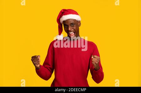 Christmas, Finally. Overjoyed Black Guy In Santa Hat Celebrating Success, Clenching Fists Stock Photo
