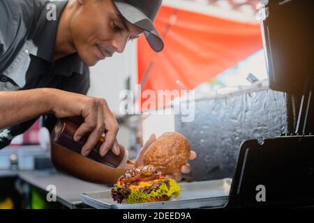Cook in a food truck or burger joint finishing a cheeseburger Stock Photo