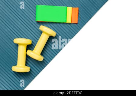 Yellow dumbbells and a set of multi-colored elastic bands for fitness on a sports mat and a white background diagonally. Stock Photo