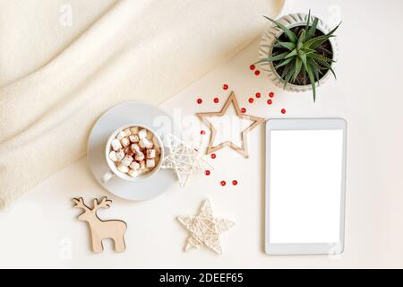 A digital tablet with a blank screen lies on a white table surrounded by flat wooden Christmas decorations Stock Photo