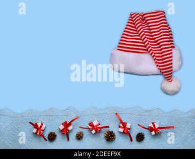 Striped hat Santa laid out on a blue background. Below, horizontally in a row, small gift wrappers and tied and golden cones on a white openwork knitt Stock Photo
