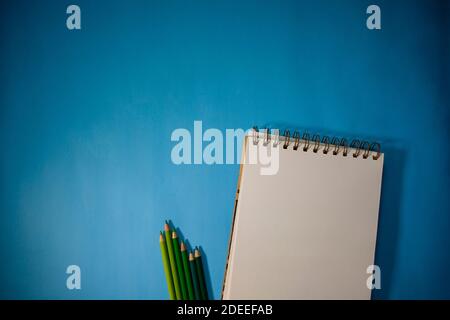 Notebook with a set of colored pencils with the range of greens. Light blue background Stock Photo