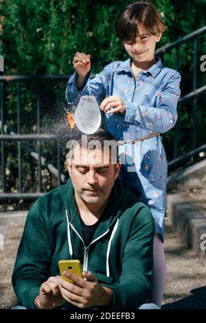 Girl blowing up a water-filled balloon over her father's head Stock Photo