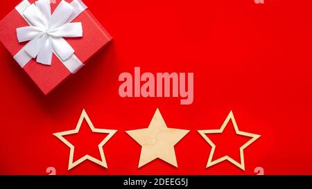 Wide Christmas banner Red gift box with a white bow in the corner, three wooden stars Stock Photo