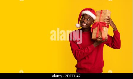 Excited Black Man In Santa Hat Shaking Wrapped Gift Box, Receiving Christmas Presents Stock Photo
