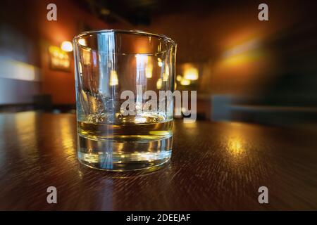 Drinking whiskey in an empty bar. Golden colour alcohol drink on wooden table in a pub. Relaxing after work, drinking booze Stock Photo