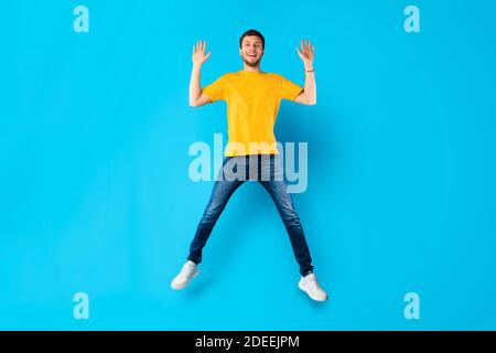 Happy guy jumping over blue studio wall Stock Photo