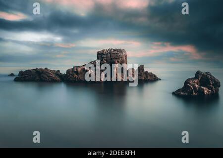 Beautiful long exposure against dramatic sunset sky on the beach with dragon rock and calm water Stock Photo
