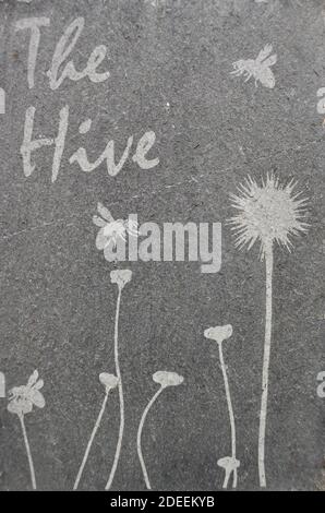 Slate bee hive artwork sign with 'The Hive' writing and flowers and bumblebees. Stock Photo