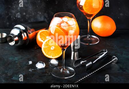 Aperol spritz cocktail in big wine glass with orange and ice, summer alcoholic cold drink, dark bar counter with steel bar tools, copy space Stock Photo