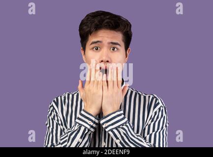 Scared asian man grimacing, shocked at purple studio Stock Photo