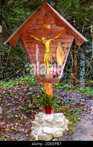 Wooden capital with crucified Jesus and flower pots on the road leading to the Gorg d'Abiss waterfall, Tiarno di Sotto (TN) Stock Photo