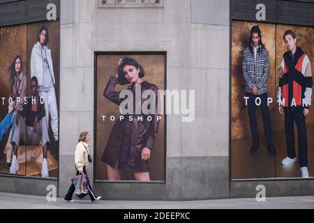 In advance of a re-opening of businesses and before a change to a Tier 2 for London during the second wave of the Coronavirus pandemic, a Londoner walks past posters at the rear of the Topshop clothing retailer which is soon expected to be placed under administration, on 30th November 2020, in London, England. Retailers will once again be open for Christmas business on 3rd December. Stock Photo