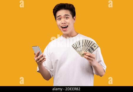 Asian guy holding mobile phone and bunch of money Stock Photo