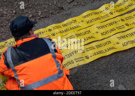 Munich, Germany. 23rd Nov, 2020. Workers are laying yellow protective tape in a construction pit in the city centre with the inscription 'Achtung - Kabelkanal - Deutsche Telekom'. The tapes serve to indicate that data cables have been laid here during subsequent construction work. Credit: Peter Kneffel/dpa/Alamy Live News Stock Photo