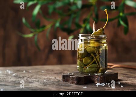 Capers. Marinated or pickled canned capers fruit in glass jar on wooden table background. Space for text Stock Photo